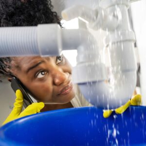 woman using a bucket to catch the water from a leaking pipe